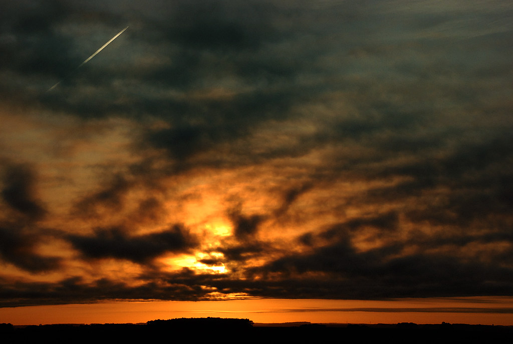 Warm dawn light breaking through heavy clouds over a dark horizon